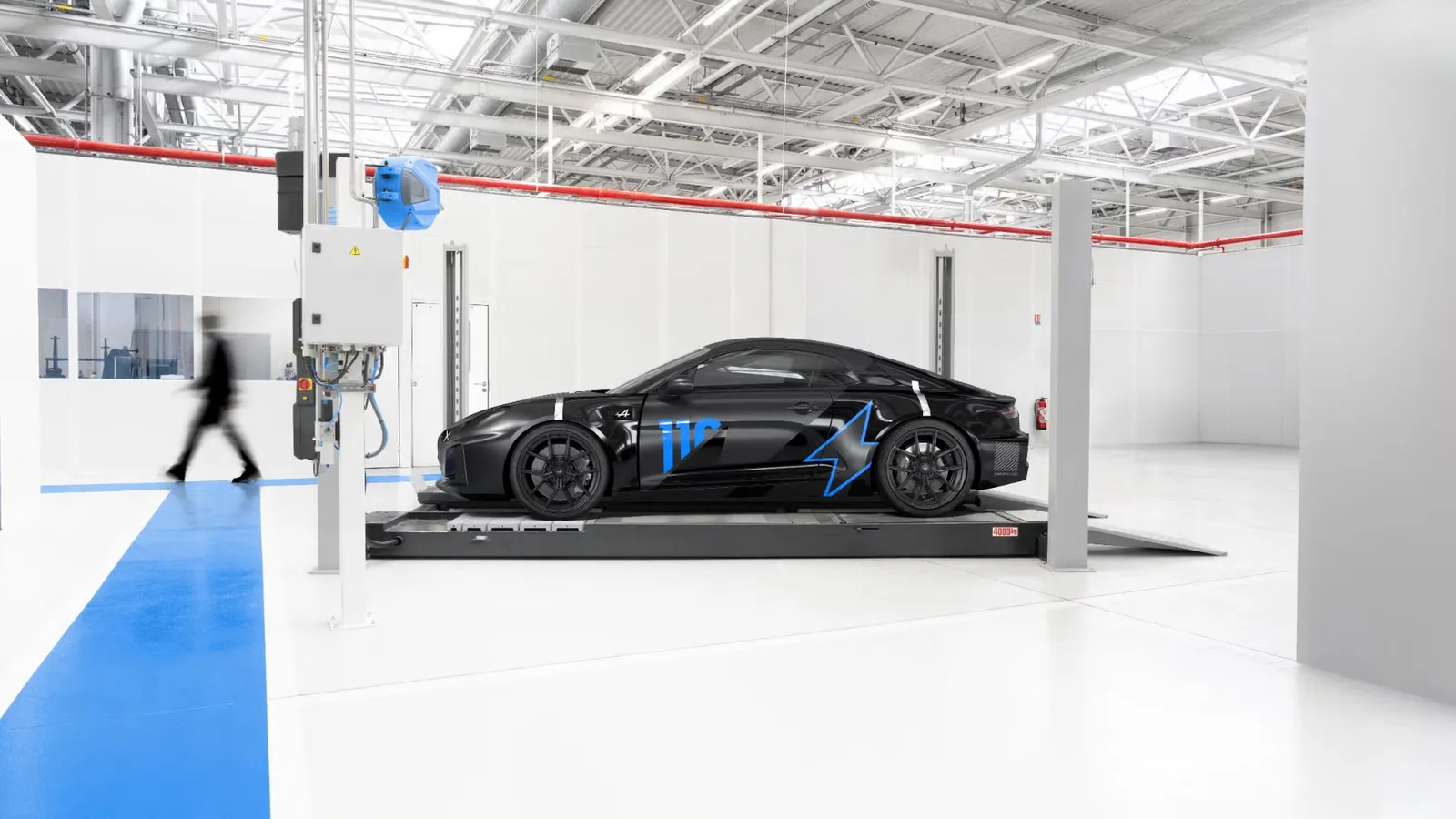 Protótipo preto do Alpine A110 elétrico com detalhes azuis, sobre um elevador numa oficina de testes